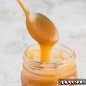 A spoon scooping caramel sauce out of a jar.