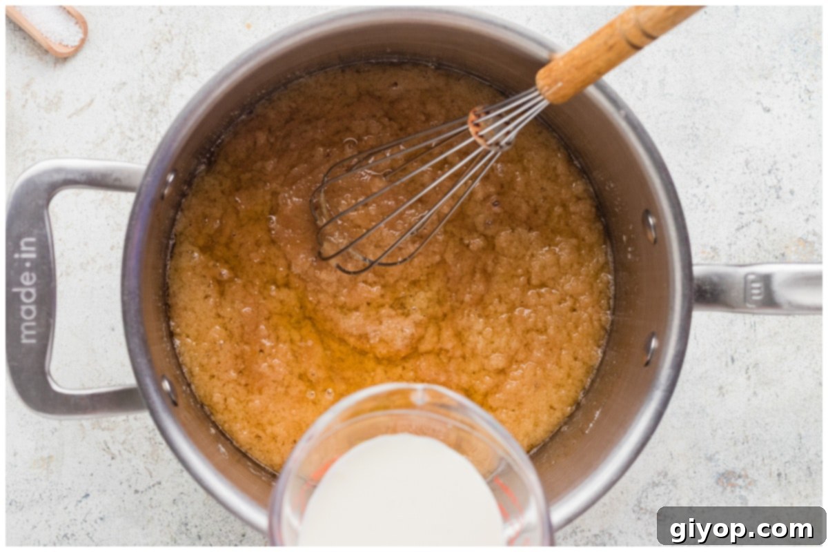 Pouring heavy cream into hot caramel in a saucepan, causing it to bubble and integrate.