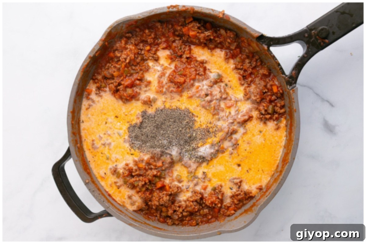 A close-up of the Bolognese meat sauce simmering in a pot, with milk recently added, creating a creamy and rich texture. Herbs are visible, contributing to the aromatic depth of the sauce.