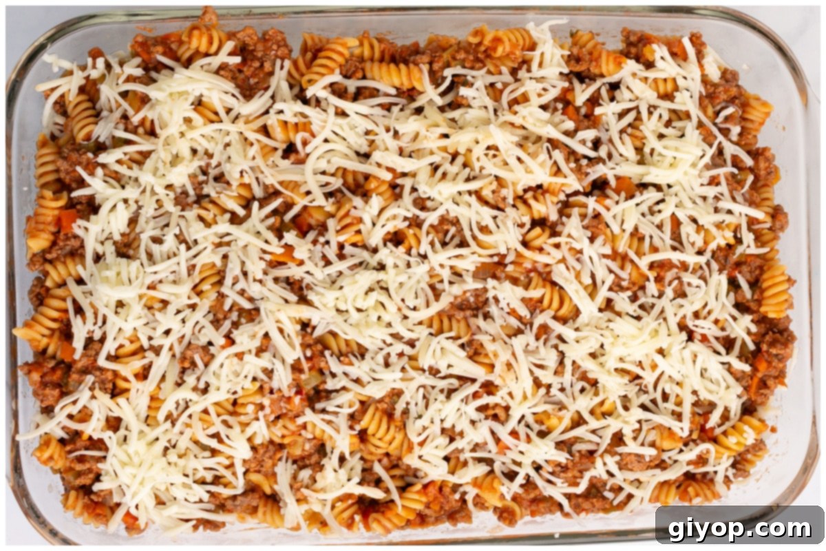 A glass baking dish filled with pasta bolognese, layered with shredded mozzarella cheese, ready to be baked in the oven until golden and bubbly.