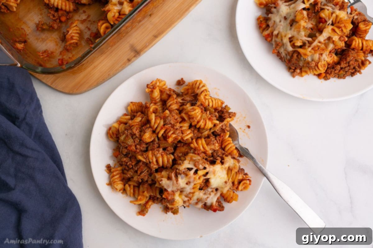 An overhead image of a white plate with a serving of baked pasta bolognese, showcasing the rich sauce, tender pasta, and melted cheese.