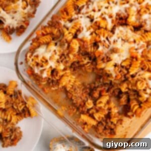 An overhead image of a glass casserole dish filled with bubbling baked pasta bolognese, topped with melted cheese.