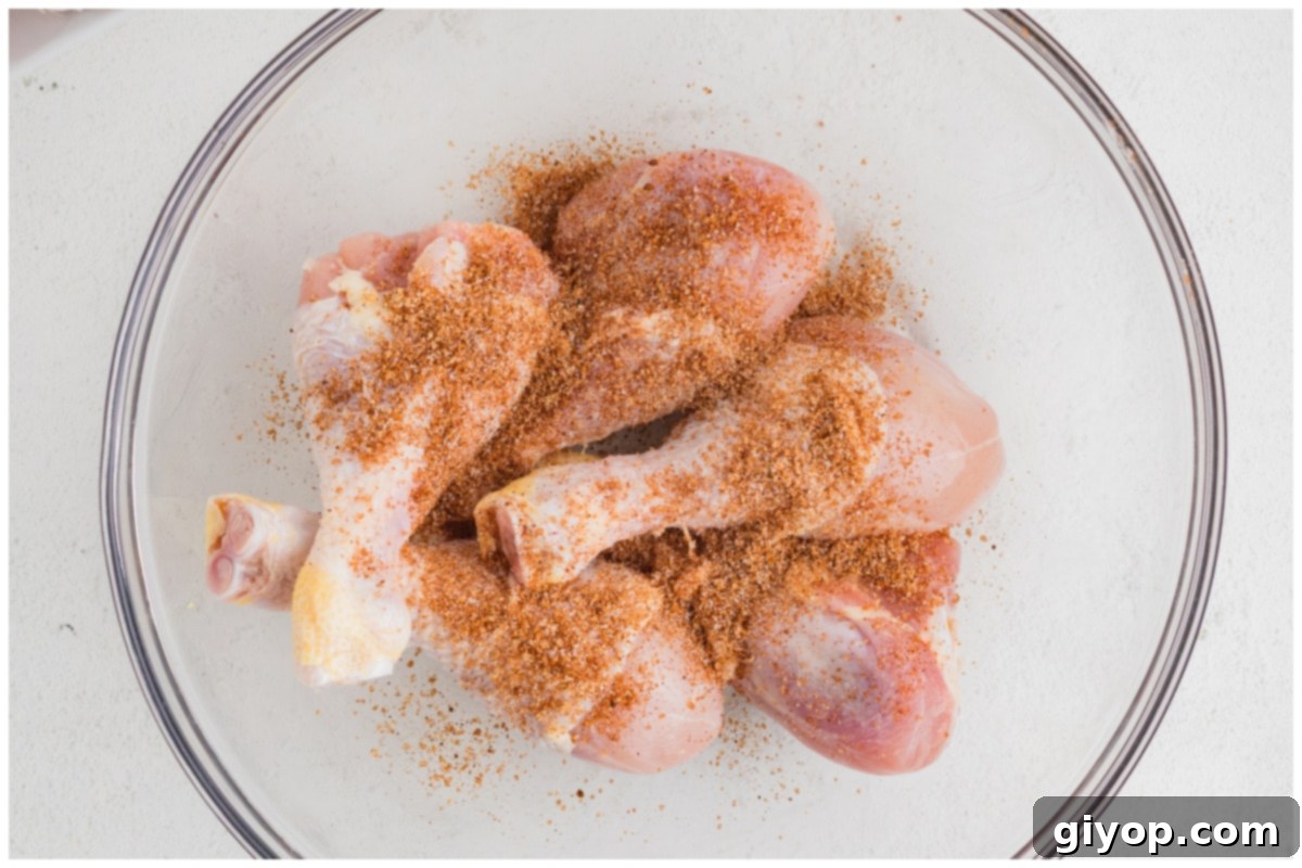 Chicken drumsticks coated in olive oil and a savory spice rub in a large glass mixing bowl.
