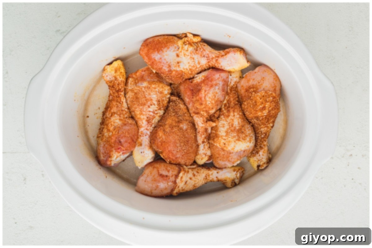 Seasoned chicken drumsticks neatly arranged in a single layer inside a slow cooker, ready for cooking.