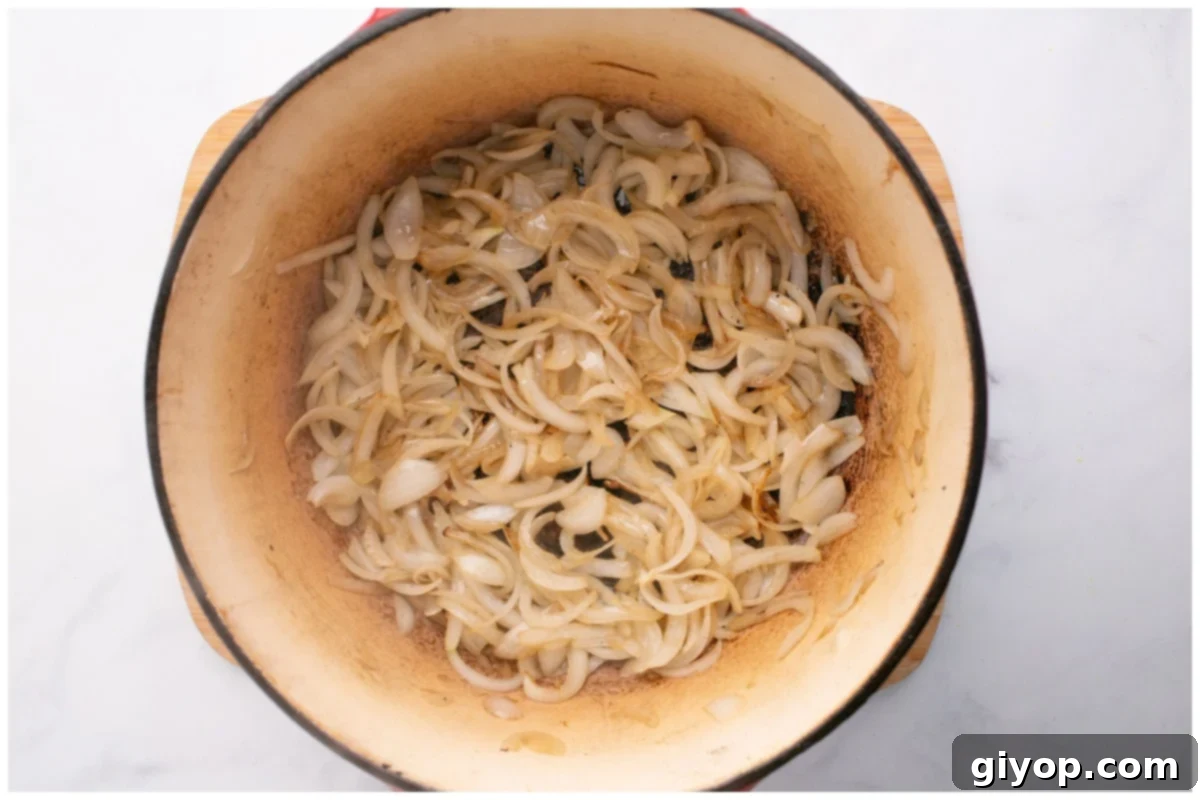 Sliced onion rings and serrano peppers gently sautéing in a pot, becoming soft and translucent.