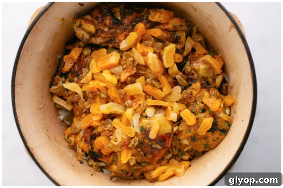 Chicken tagine ingredients, including seared chicken, onions, apricots, and raisins, simmering gently in a deep pot with a rich, aromatic sauce.