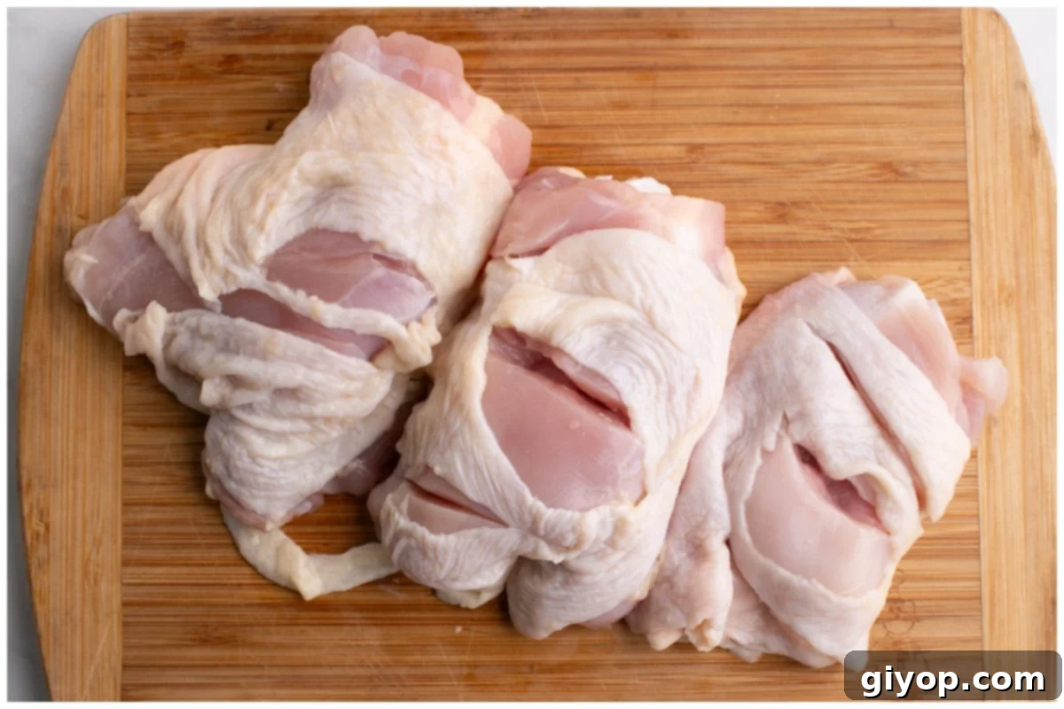 Close-up image of bone-in, skin-on chicken thighs on a wooden board with shallow cuts, prepared for marination.