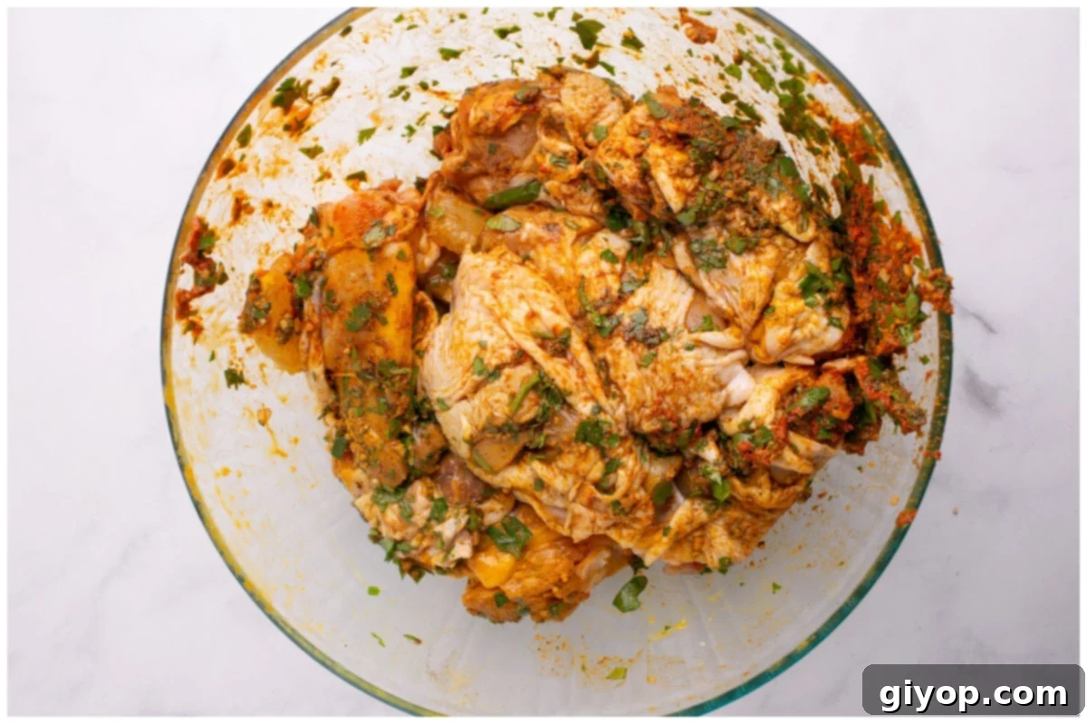 Marinated chicken thighs covered in a rich, spiced mixture, resting in a glass bowl, absorbing the flavors.