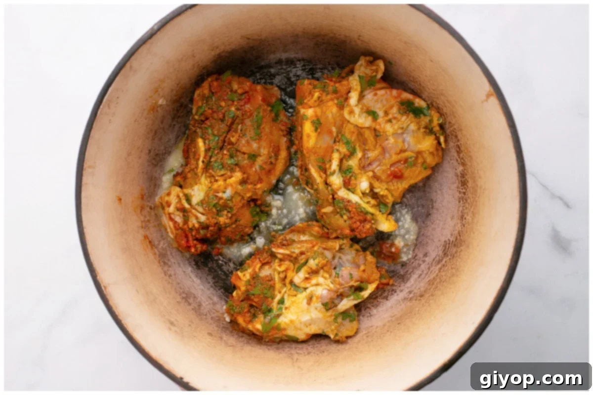 Chicken thighs searing in a deep Dutch oven, achieving a golden-brown crust before being removed.