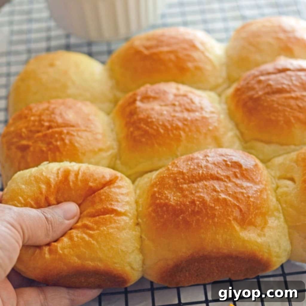 A hand pulling a piece of fluffy dinner roll from a stack, showcasing its softness.
