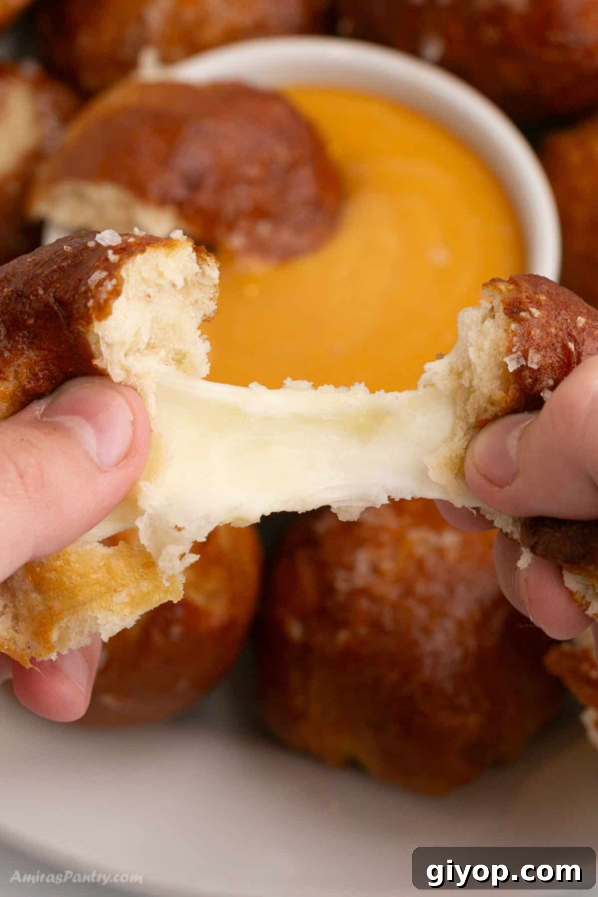 Hands pulling one pretzel apart showing melty cheese. Highlighting the gooey center.