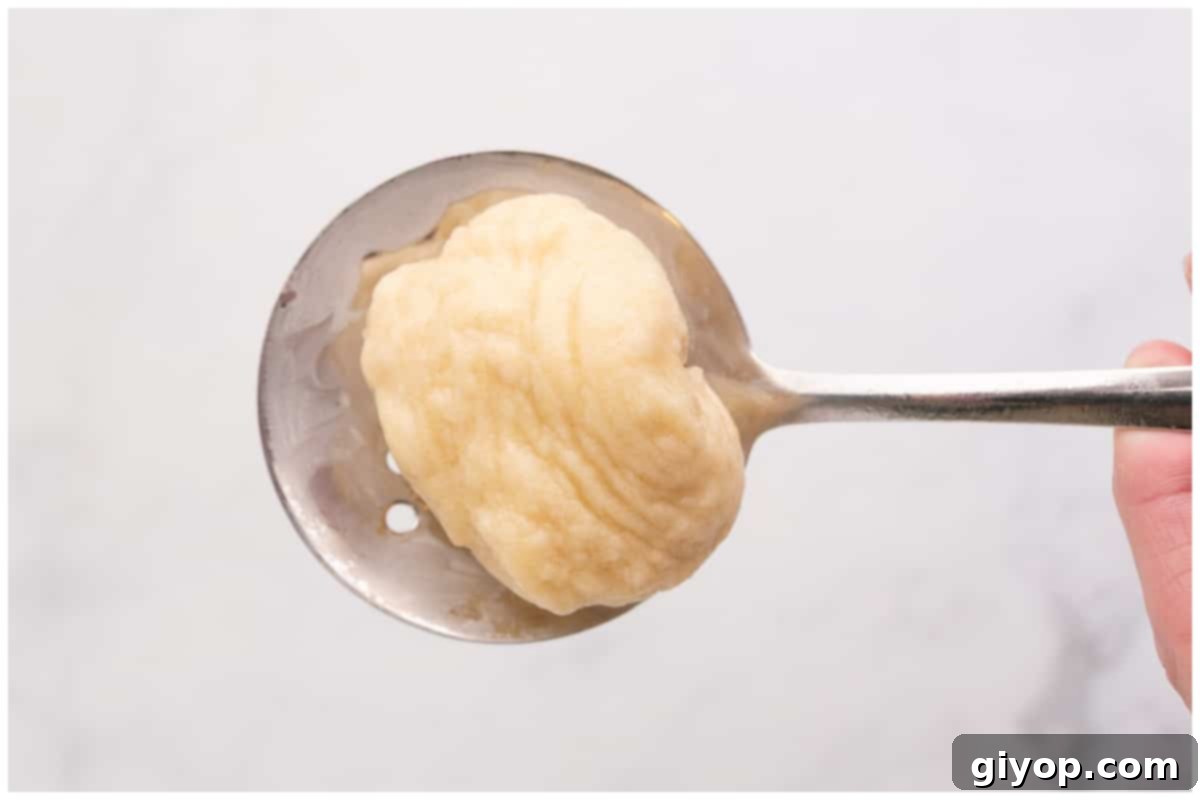 A hand holding a slotted spoon, carefully removing a boiled dough ball from a pot of boiling water.