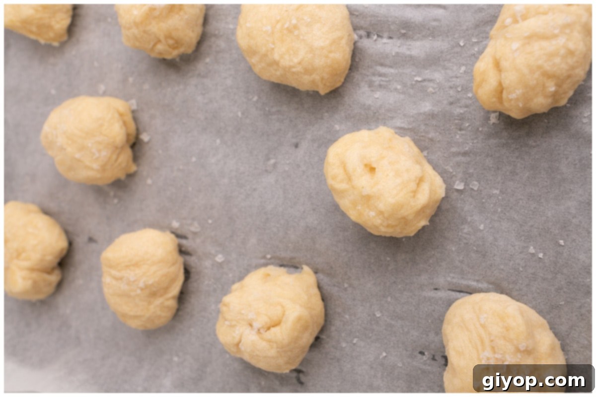 Freshly boiled pretzel dough balls, salted and arranged neatly on a baking sheet lined with parchment paper, ready for baking.