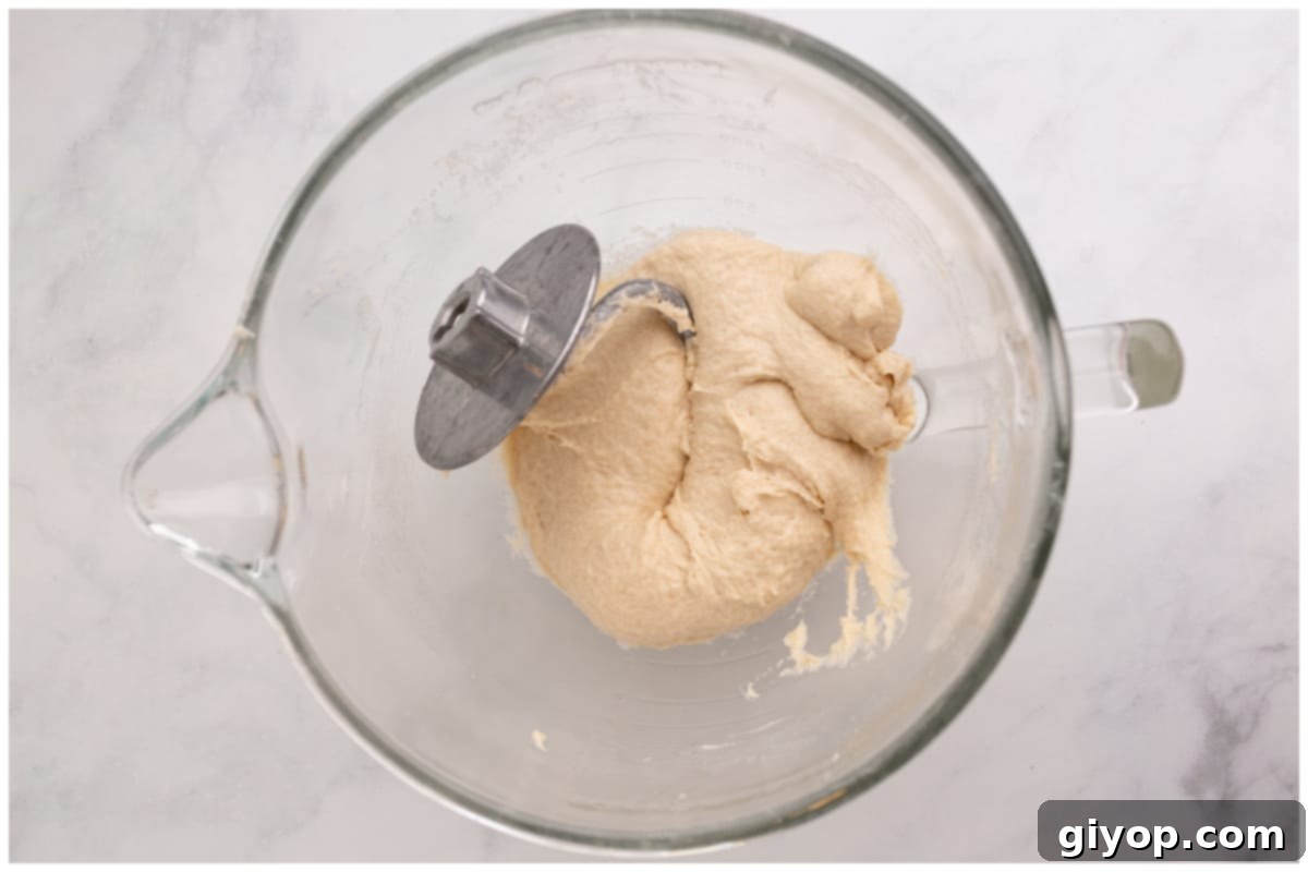 A stand mixer bowl with pretzel dough being kneaded by a dough hook, showing the developing consistency.