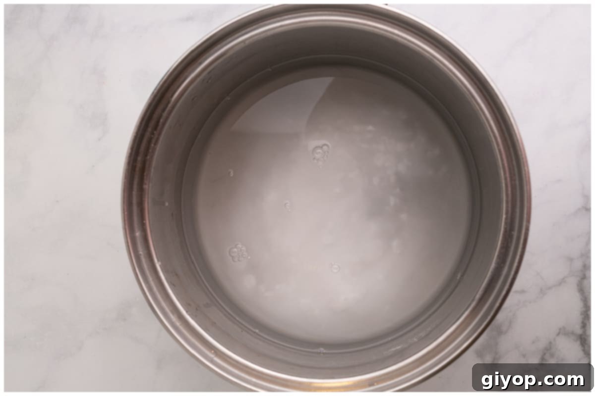 A large pot of water and baking soda vigorously boiling on a stovetop, ready for the pretzel bath.