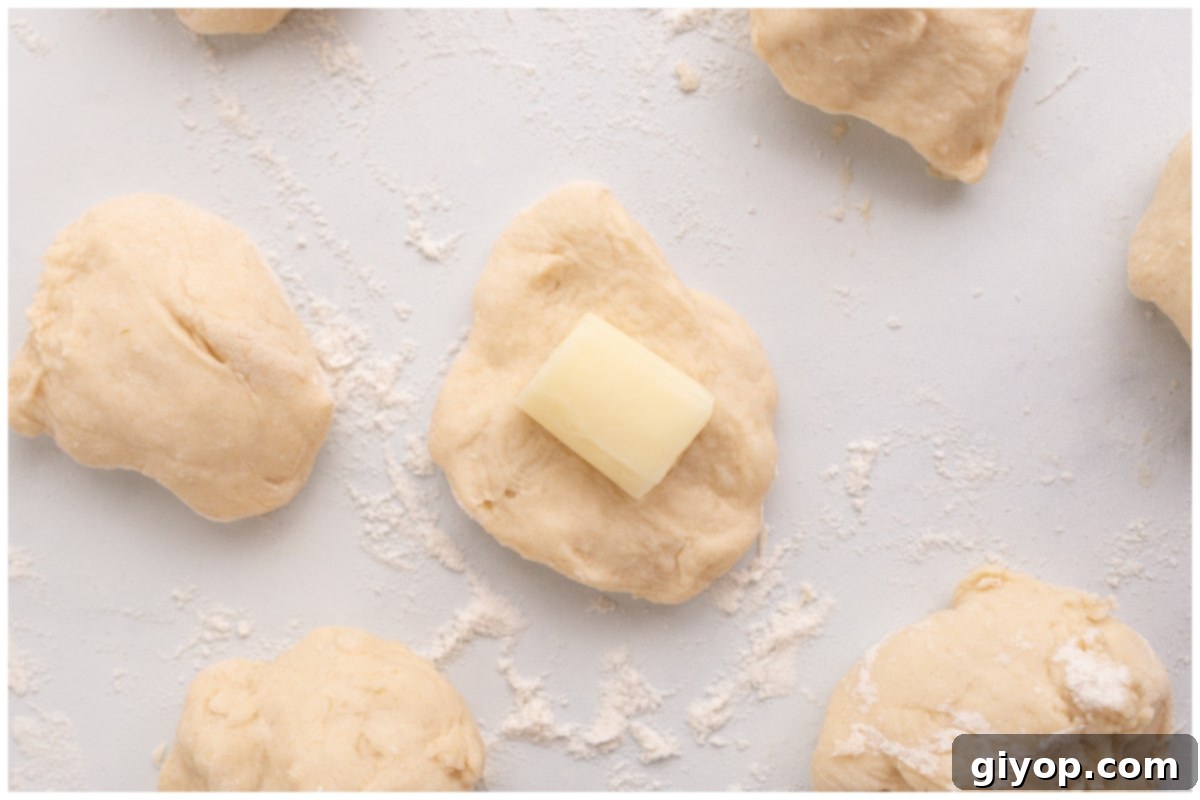 Pretzel dough balls resting on a surface, with one ball opened to show a piece of mozzarella cheese being placed inside.