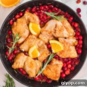 Zesty Cranberry Orange Chicken 5 An overhead image of a skillet with orange cranberry chicken garnished with rosemary.