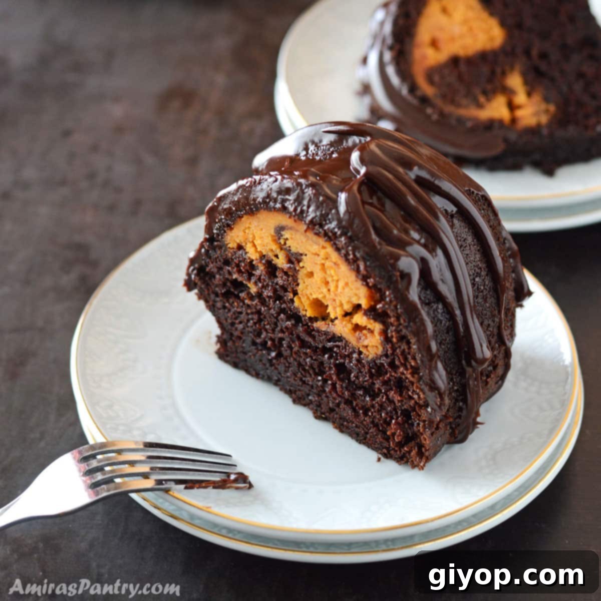 A beautifully presented slice of Chocolate Pumpkin Bundt Cake on a small dessert plate, showing the chocolate layers and the vibrant pumpkin cream cheese swirl.