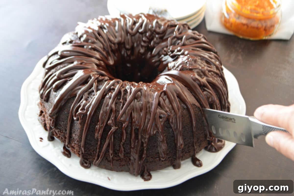 A hand gently cutting a perfect slice of the Chocolate Pumpkin Bundt Cake, revealing the beautiful layers of chocolate cake and pumpkin cream cheese filling.