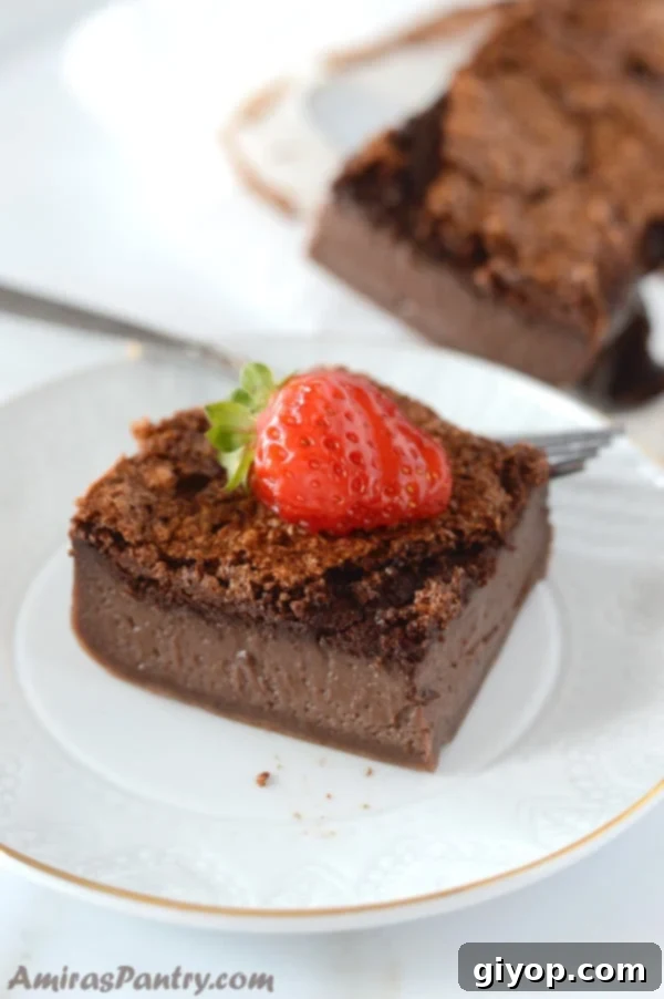 A slice of Chocolate Magic Cake, revealing its three distinct layers, served on a white plate with fresh strawberries on the side.