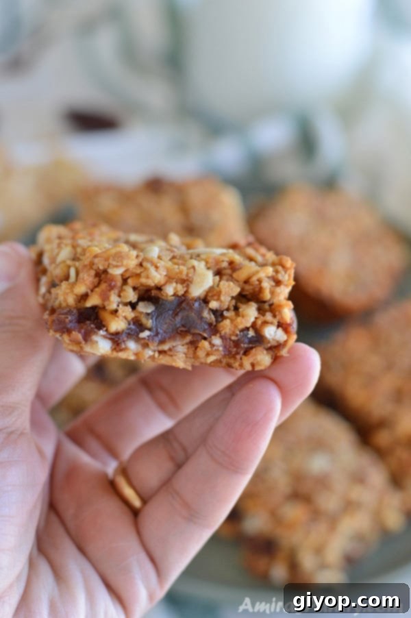 A hand holding one of the breakfast squares, showcasing its crunchy texture and the delicious date paste filling.