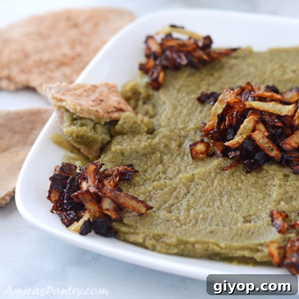 Green bissara dip on a white plate and garnished with fried onions.