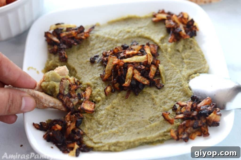 A hand scooping up some bissara dip with pita bread