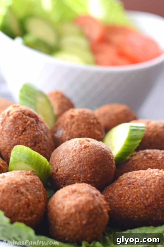 A big serving plate with kibbeh on a table with another plate of cucumber and tomato slices.