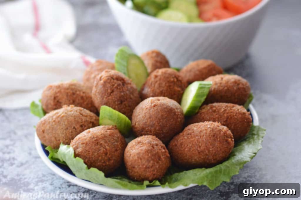 A blue plate with kibbeh on a bed of lettuce with cucumber slices and a plate of tomato slices and cucumbers in the back.