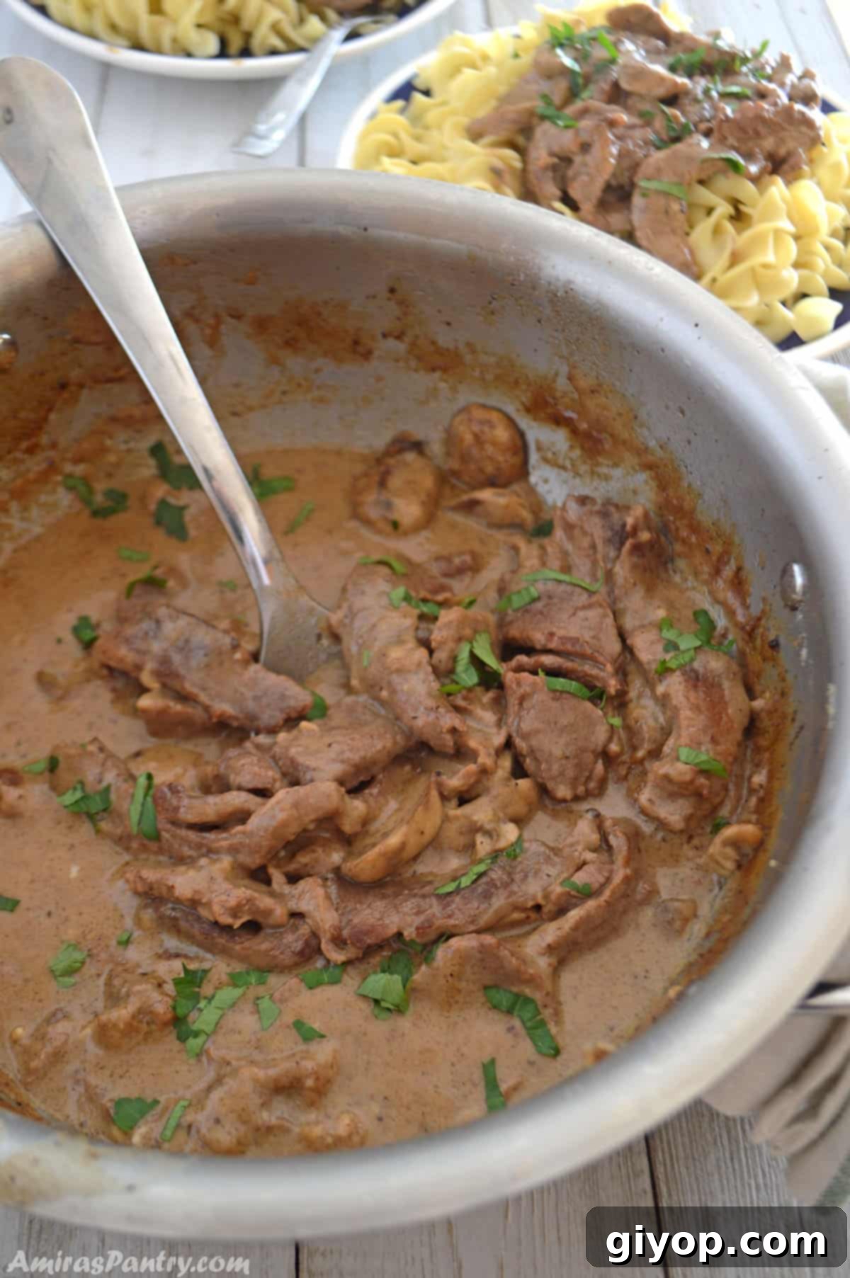 A pan filled with savory beef stroganoff, with a serving spoon resting in the rich, creamy sauce.