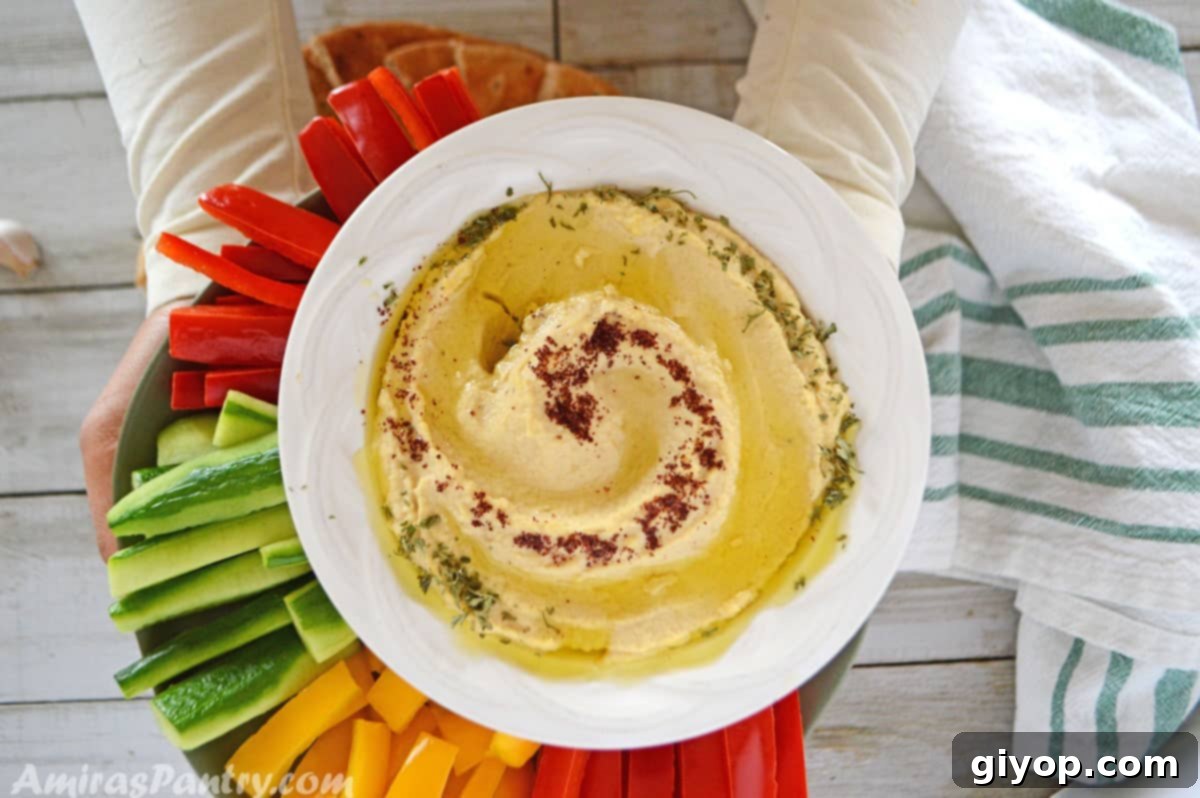 Hands holding a serving platter adorned with creamy hummus and an assortment of fresh, colorful vegetables, showcasing a delightful and healthy snack.