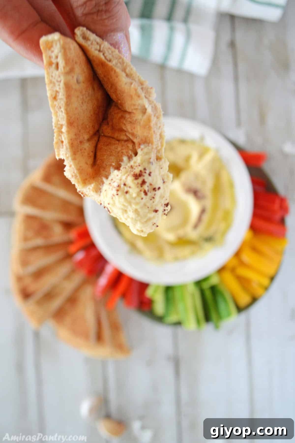 A hand holds a piece of warm pita bread, perfectly dipped into a bowl of creamy, homemade hummus, inviting a taste.