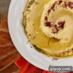 A beautifully presented white bowl filled with creamy, smooth hummus, garnished and ready to be served.