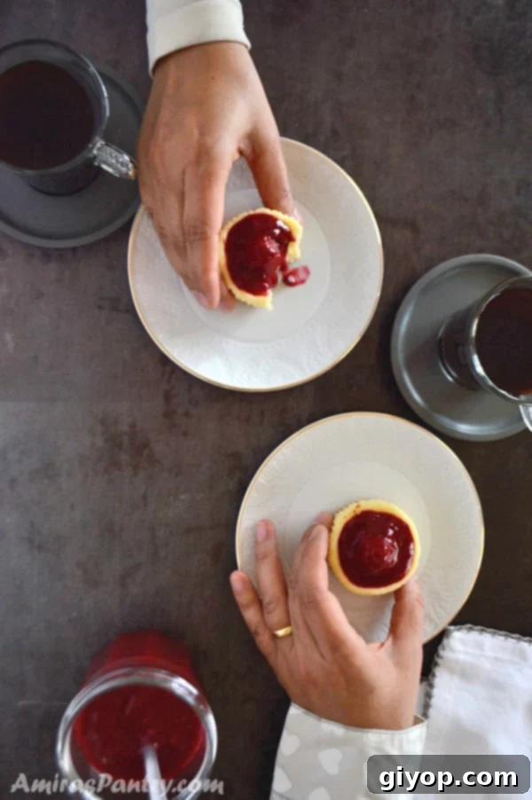 Raspberry Cheesecake Bites 4 The image captures two hands reaching for mini raspberry cheesecakes, perfectly paired with cups of coffee, highlighting a cozy and inviting moment of enjoying a sweet treat.