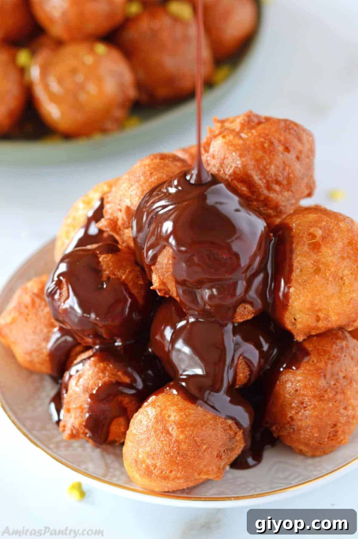 Chocolate ribbons being poured over a white plate of loukoumades.