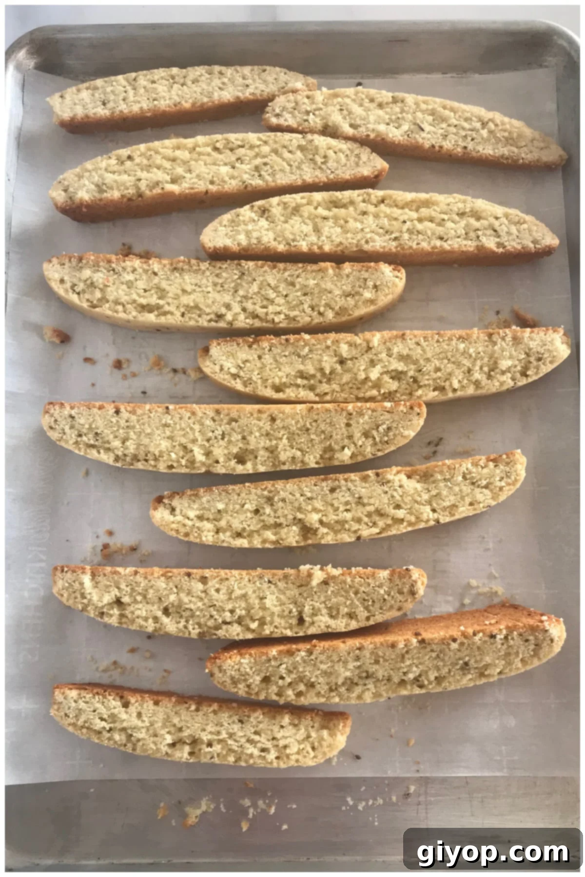 Golden-brown anise biscotti slices neatly arranged on a baking sheet, poised for their second bake to achieve ultimate crispness.