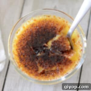 Decadent Vanilla Bean Creme Brulee 2 A glass ramekin with creme brulee with a spoon in it.
