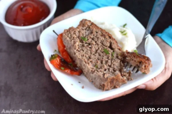 Hands holding a plate with two perfectly sliced pieces of moist beef meatloaf, showing the tender interior and delicious glaze.