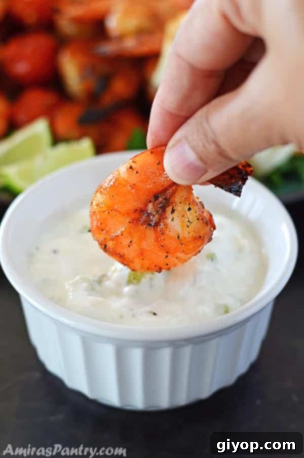 Zesty Grilled Shrimp Skewers 3 A hand dipping a perfectly grilled shrimp skewer into a creamy yogurt sauce, highlighting the succulent texture.