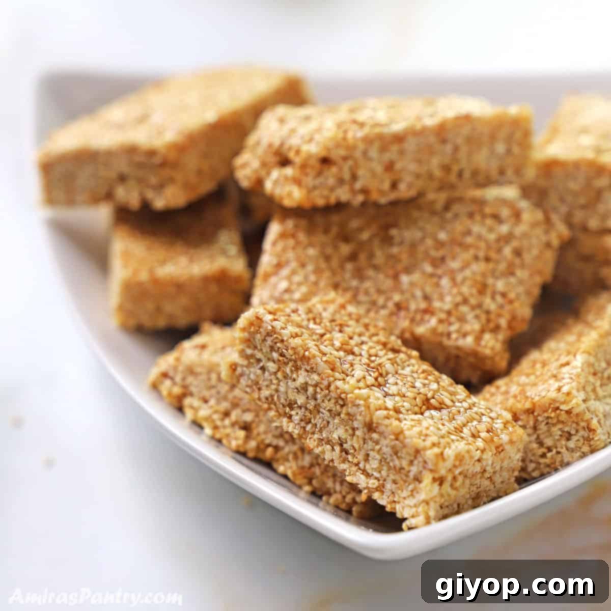 A stack of golden brown sesame candy bars arranged beautifully on a pristine white plate, showcasing their rich texture and golden hue.