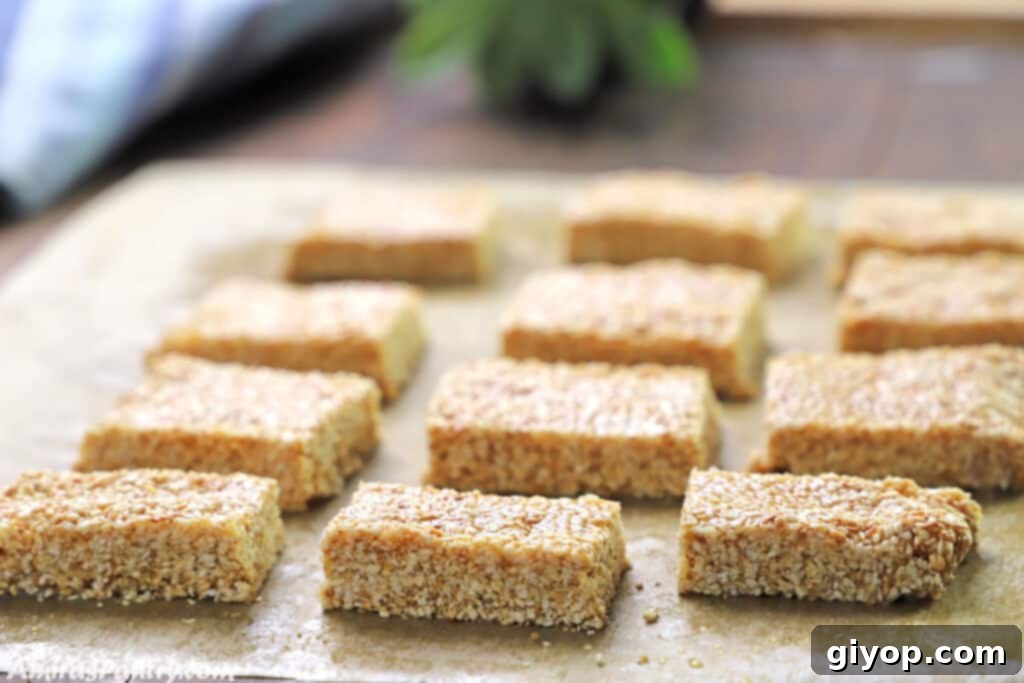 Freshly made sesame bars resting on a sheet of parchment paper, beautifully arranged on a rustic wooden board, ready for enjoyment.