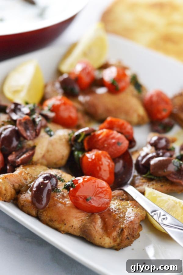 A plate of golden-brown baked lemon pepper chicken, generously topped with a vibrant relish of Kalamata olives and charred grape tomatoes, garnished with fresh parsley.