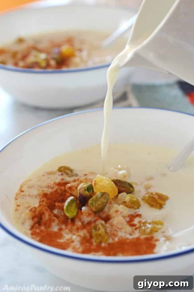pouring milk from a milk pitcher on a white bowl with wheat berries and garnished with nuts, raisins and cinnamon.