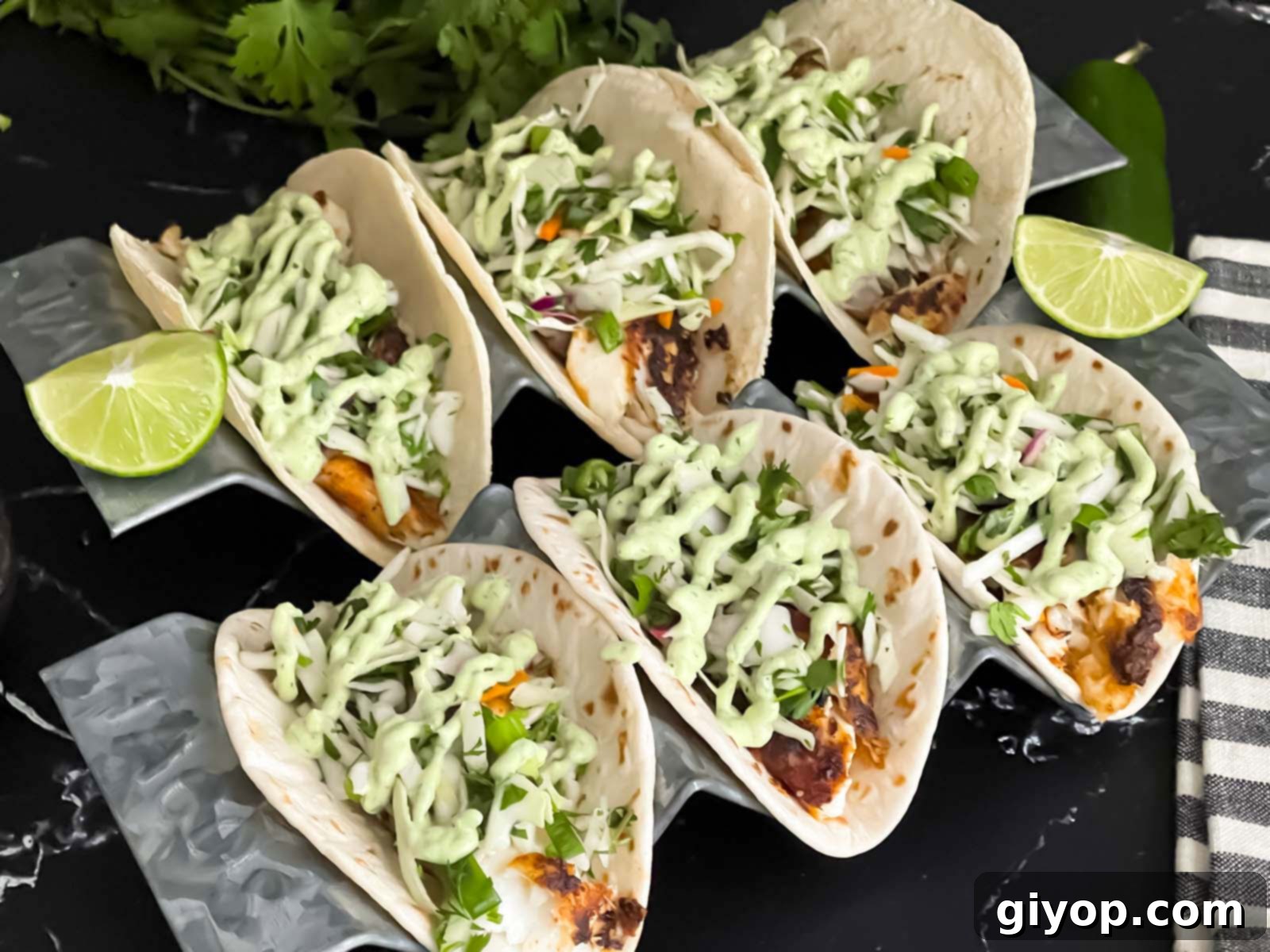 Fiery Blackened Fish Tacos 2 Blackened Fish Tacos on a dark background, garnished with fresh cilantro and lime wedges.