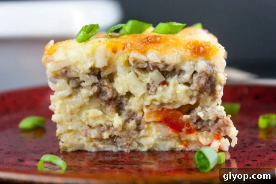 A slice of golden-brown sausage hashbrown breakfast casserole on a vibrant red plate, garnished with fresh green onions.