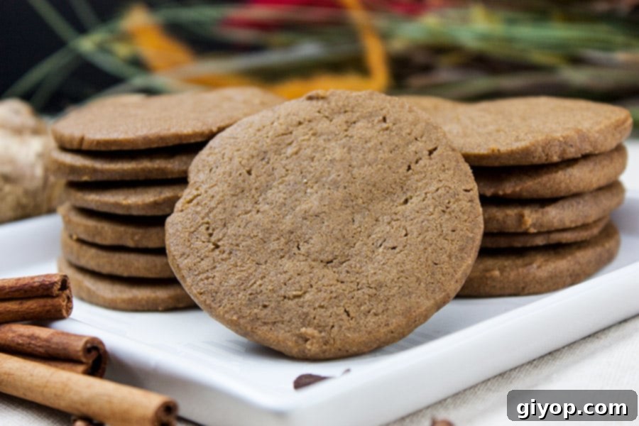 Stacked crispy gingersnap cookies on a white plate, showcasing their inviting texture and golden-brown hue.
