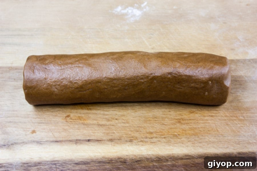 Gingersnap cookie dough rolled into a perfect log shape on a wooden cutting board, ready for chilling.