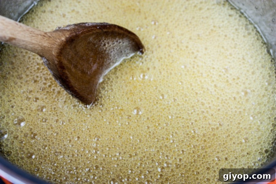 A saucepan on the stove with sugar, water, and corn syrup boiling, beginning to caramelize into a rich candy base.