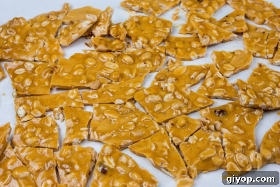 Crispy peanut brittle broken into irregular, delicious pieces, scattered on parchment paper.