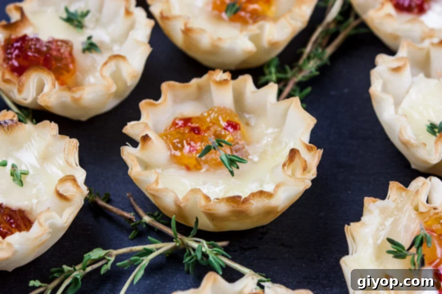 Close up of a single Pepper Jelly Brie Bite on a slate platter, garnished with a sprig of fresh thyme.